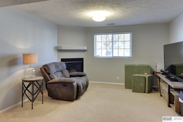 sitting room with baseboards, visible vents, carpet floors, a textured ceiling, and a glass covered fireplace