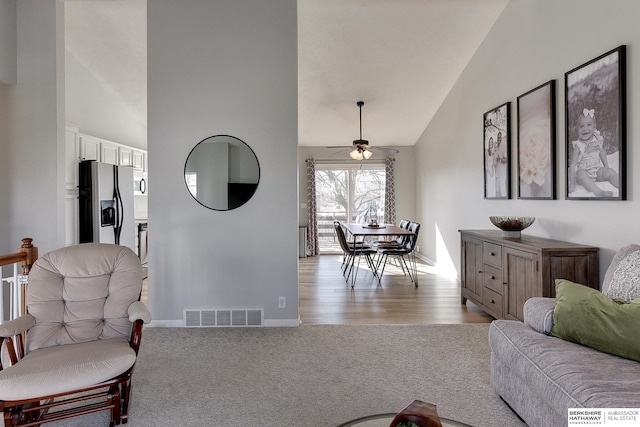 living area with visible vents, high vaulted ceiling, a ceiling fan, baseboards, and light colored carpet