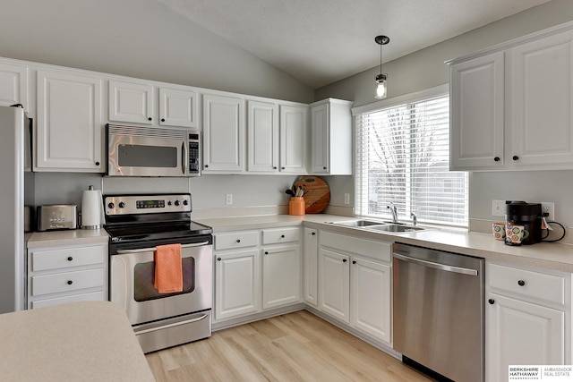 kitchen with light wood-type flooring, light countertops, lofted ceiling, stainless steel appliances, and a sink