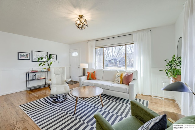 living area with wood finished floors, visible vents, and wainscoting