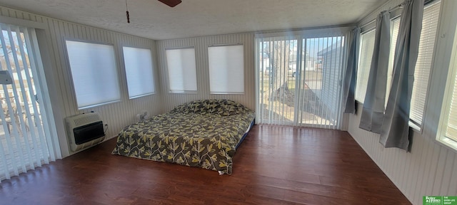 bedroom with heating unit, multiple windows, wood finished floors, and a textured ceiling