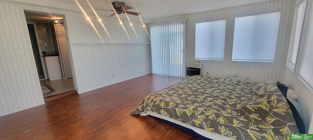 bedroom with heating unit, a textured ceiling, wood finished floors, and a ceiling fan