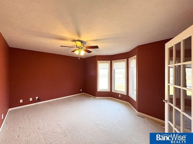 carpeted spare room featuring visible vents, baseboards, a textured ceiling, and a ceiling fan