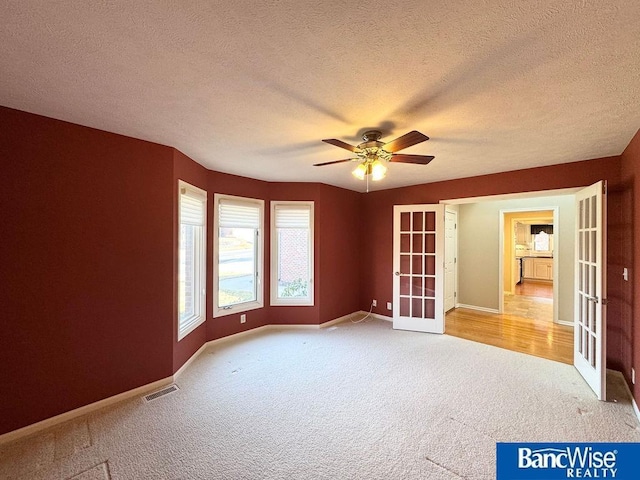 carpeted spare room featuring a ceiling fan, visible vents, baseboards, french doors, and a textured ceiling