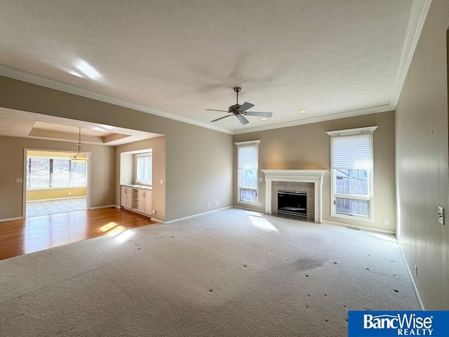 unfurnished living room featuring baseboards, a fireplace, ceiling fan, ornamental molding, and carpet flooring