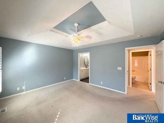 unfurnished bedroom with a raised ceiling, baseboards, and ensuite bathroom