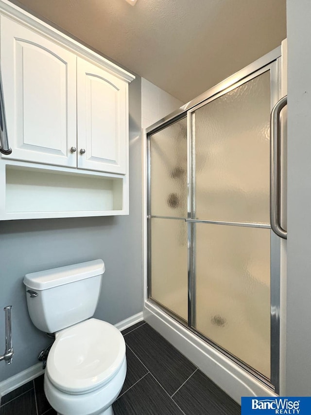 bathroom with a stall shower, toilet, and baseboards