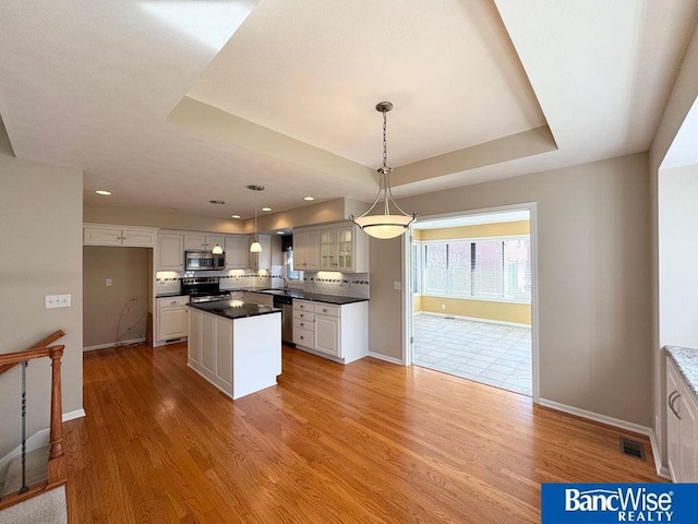 kitchen with visible vents, light wood-style flooring, a tray ceiling, dark countertops, and appliances with stainless steel finishes