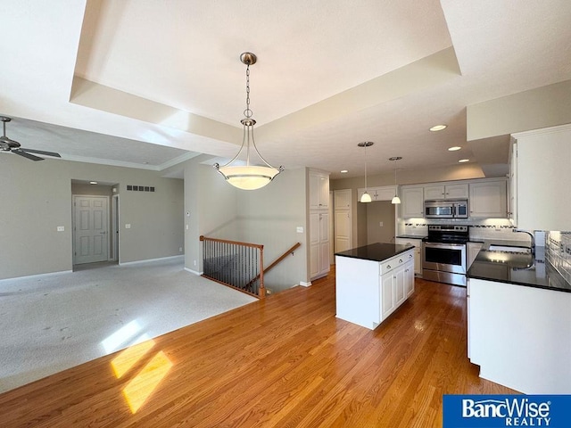 kitchen featuring stainless steel appliances, a raised ceiling, dark countertops, and visible vents