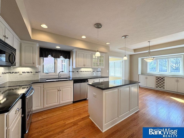 kitchen featuring dark countertops, appliances with stainless steel finishes, a raised ceiling, and a sink