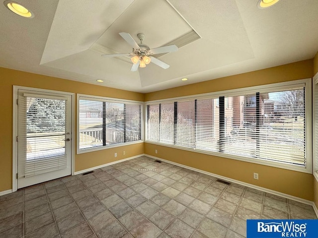 unfurnished sunroom featuring visible vents, a raised ceiling, and a ceiling fan