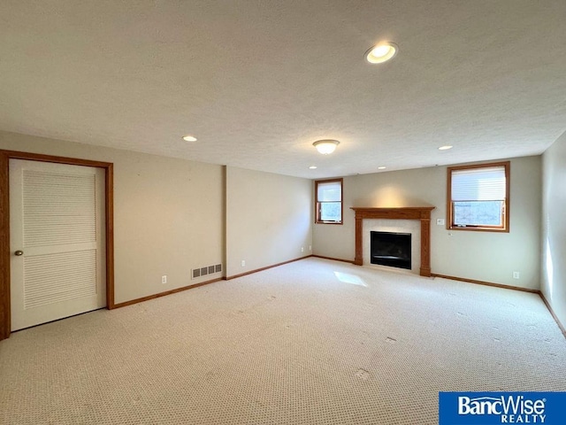 unfurnished living room with visible vents, a textured ceiling, recessed lighting, a fireplace, and baseboards