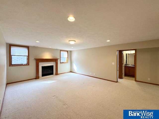 unfurnished living room featuring a wealth of natural light, baseboards, a textured ceiling, and a fireplace with flush hearth