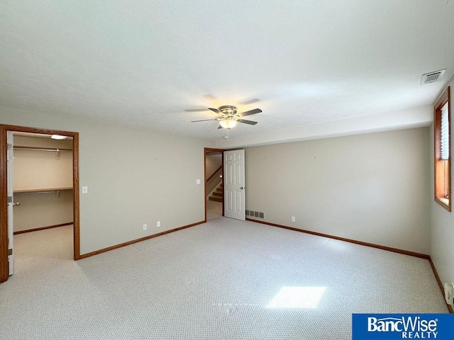 carpeted empty room featuring visible vents, a ceiling fan, stairs, and baseboards