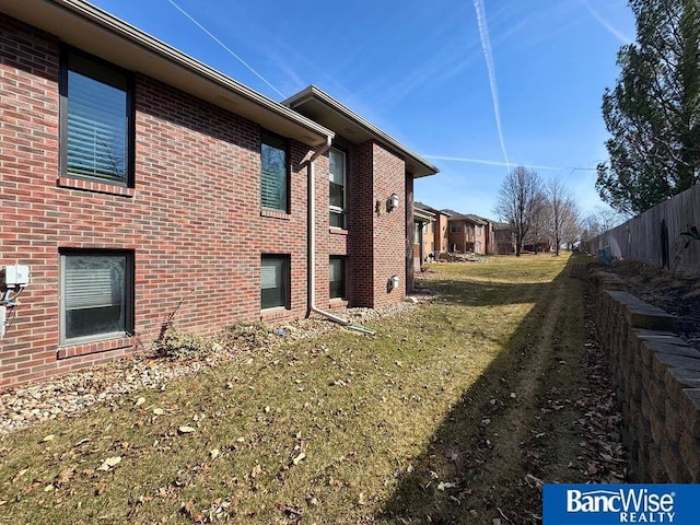 view of side of property with brick siding, a yard, and fence