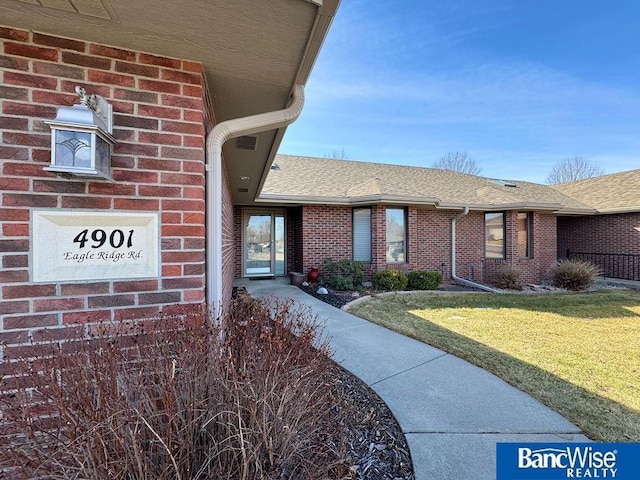 property entrance with brick siding, a yard, and roof with shingles