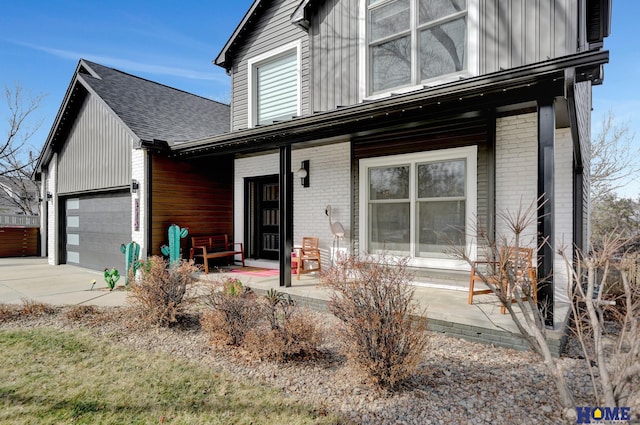 view of front of home featuring board and batten siding, covered porch, concrete driveway, an attached garage, and brick siding