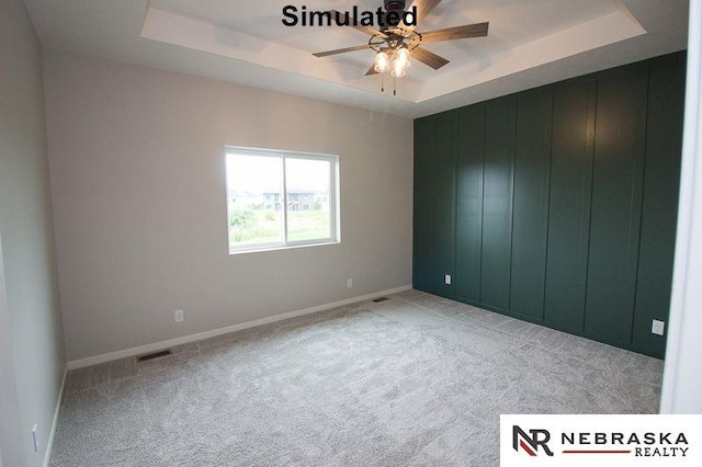 carpeted empty room featuring visible vents, a raised ceiling, baseboards, and a ceiling fan