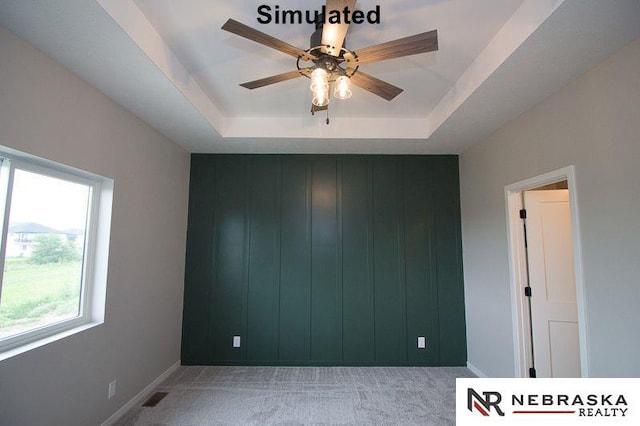 carpeted spare room with wooden walls, visible vents, baseboards, a tray ceiling, and a ceiling fan