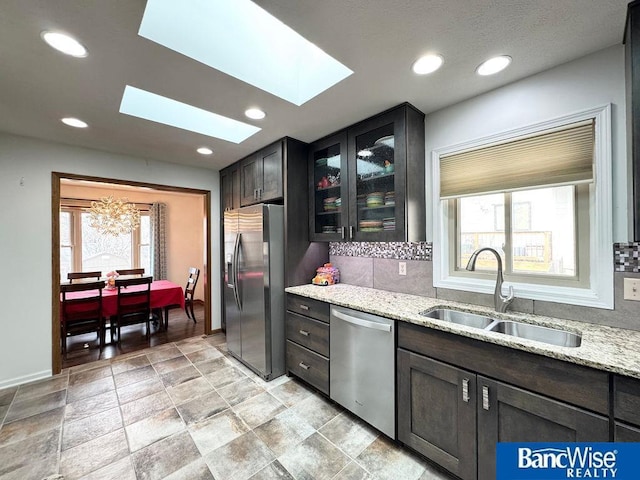 kitchen featuring a skylight, a sink, glass insert cabinets, appliances with stainless steel finishes, and tasteful backsplash