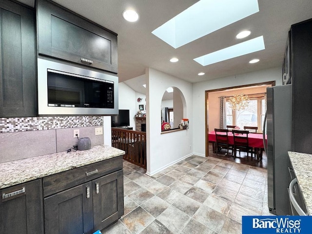 kitchen with light stone counters, recessed lighting, stainless steel appliances, a skylight, and decorative backsplash