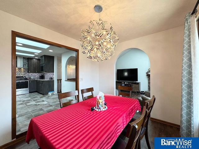 dining space featuring arched walkways, baseboards, an inviting chandelier, and wood finished floors