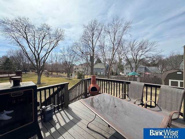 wooden terrace featuring an outbuilding, outdoor dining area, a yard, a storage unit, and a residential view