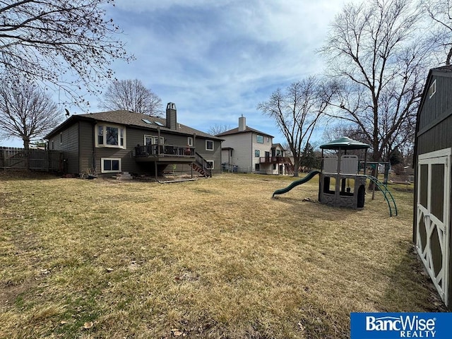 view of yard featuring a wooden deck, a playground, and fence