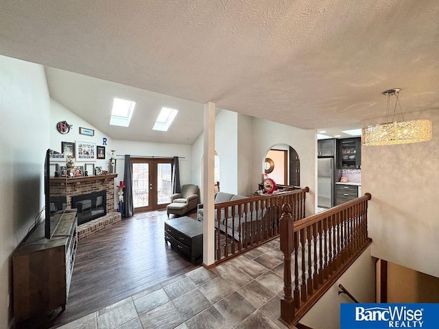 living room featuring french doors, lofted ceiling with skylight, a textured ceiling, and a brick fireplace