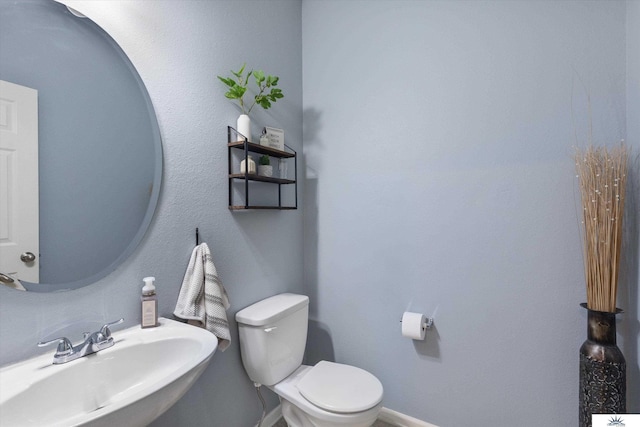 half bathroom with a sink, baseboards, and toilet