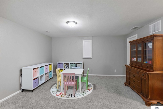 recreation room with a textured ceiling, baseboards, visible vents, and light carpet