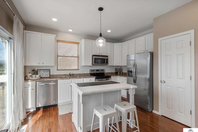 kitchen with a center island, wood finished floors, white cabinets, stainless steel appliances, and a sink