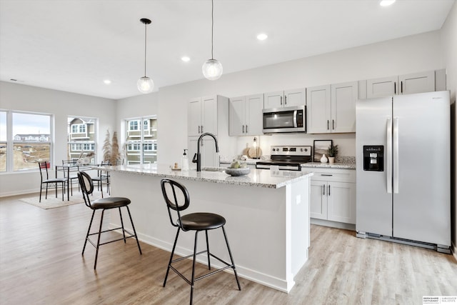 kitchen with a center island with sink, light wood-style flooring, a sink, appliances with stainless steel finishes, and a kitchen breakfast bar