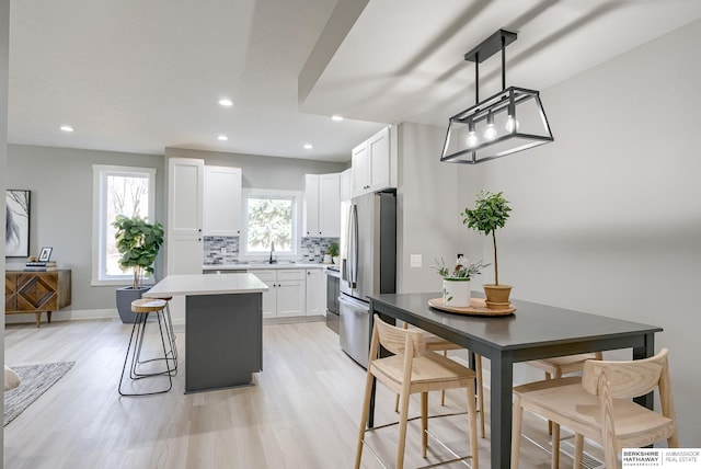 kitchen featuring freestanding refrigerator, a sink, decorative backsplash, white cabinetry, and a center island