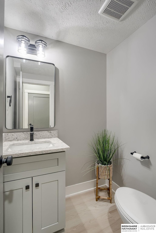 bathroom with visible vents, toilet, a textured ceiling, baseboards, and vanity