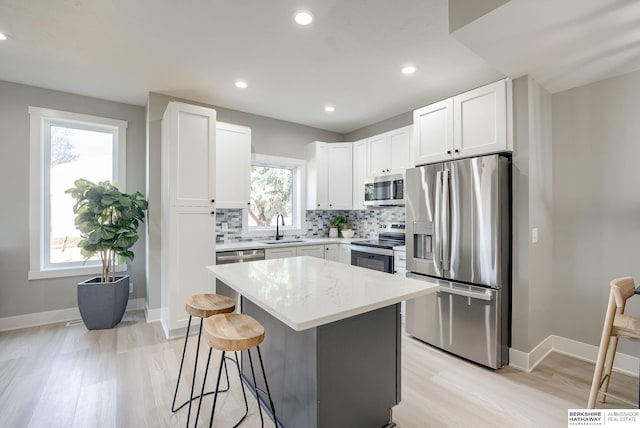 kitchen featuring a breakfast bar, a sink, backsplash, stainless steel appliances, and baseboards