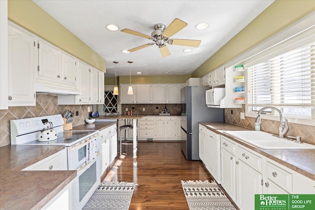 kitchen featuring a sink, under cabinet range hood, white cabinets, white appliances, and dark wood-style flooring