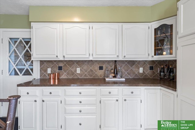 kitchen featuring dark countertops, white cabinetry, glass insert cabinets, and tasteful backsplash