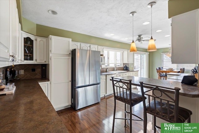 kitchen featuring white appliances, dark wood-style flooring, a sink, white cabinetry, and dark countertops