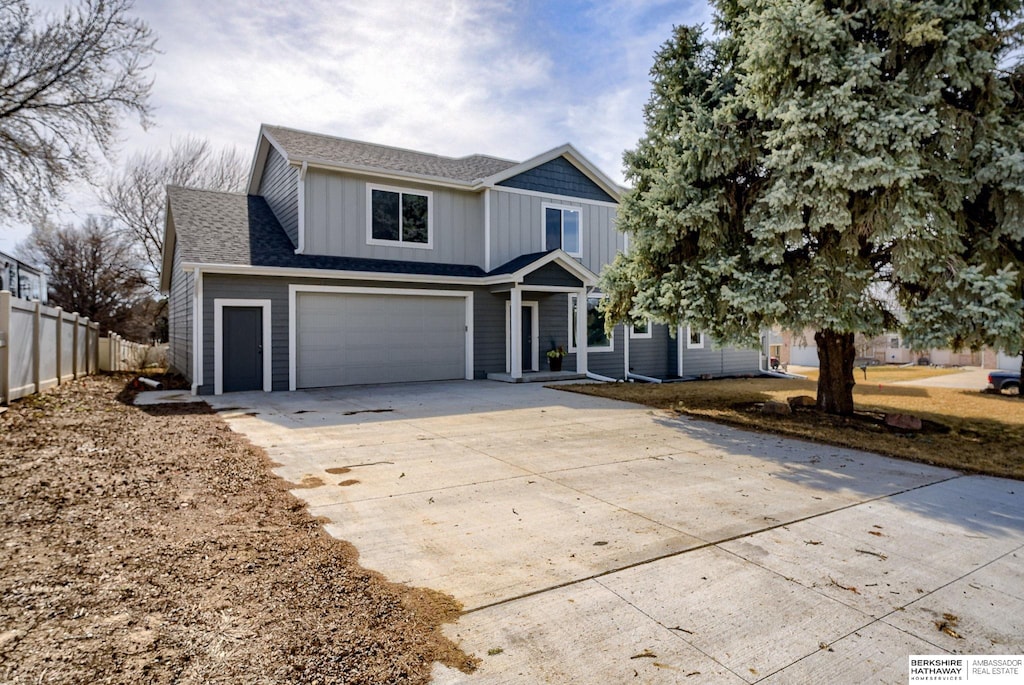 traditional-style home with fence, roof with shingles, concrete driveway, a garage, and board and batten siding