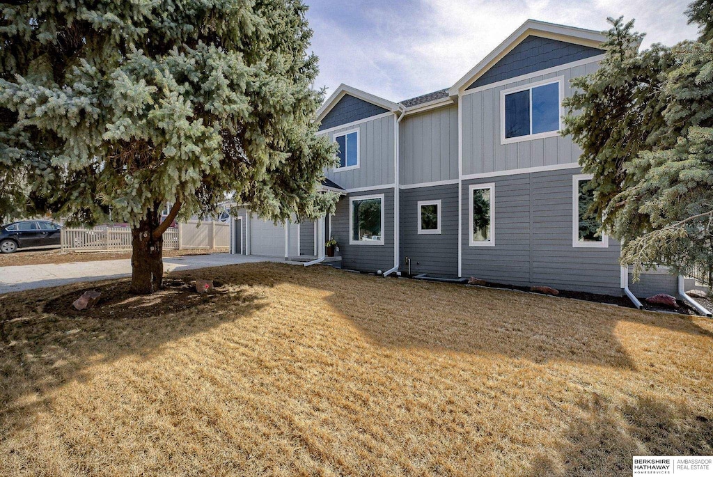 view of front of home featuring fence, driveway, an attached garage, a front lawn, and board and batten siding