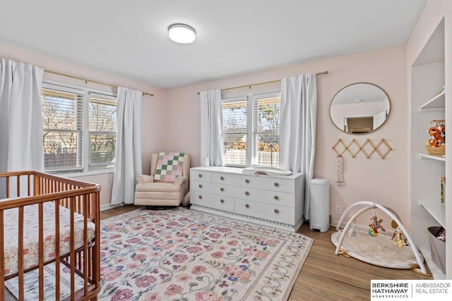 bedroom featuring baseboards, a crib, and wood finished floors