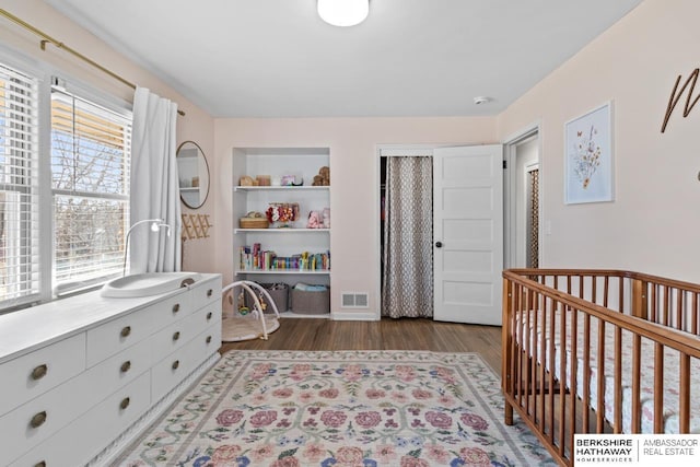 bedroom with visible vents, a nursery area, and wood finished floors