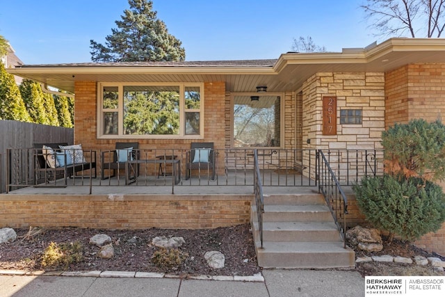 doorway to property with a porch, fence, and brick siding