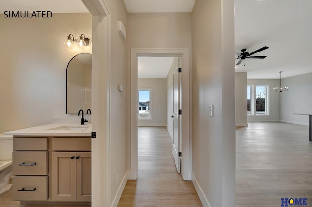 hallway with a sink, a chandelier, baseboards, and light wood-style flooring