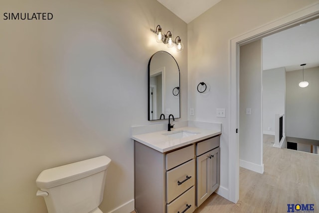 bathroom with toilet, vanity, baseboards, and wood finished floors