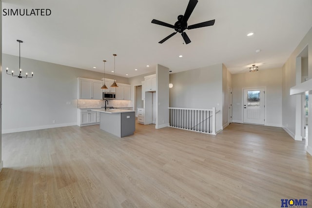 unfurnished living room with ceiling fan with notable chandelier, recessed lighting, baseboards, and light wood finished floors