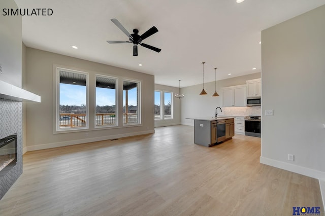 living area featuring light wood-style flooring, ceiling fan with notable chandelier, recessed lighting, a fireplace, and baseboards