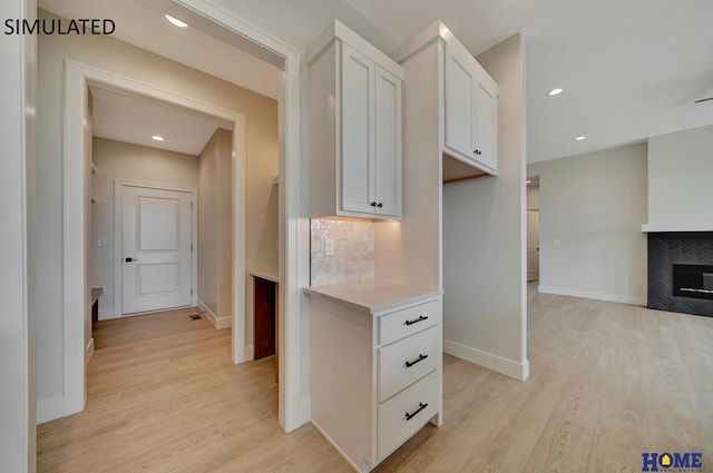 kitchen featuring light wood-style flooring, backsplash, white cabinetry, a fireplace, and light countertops