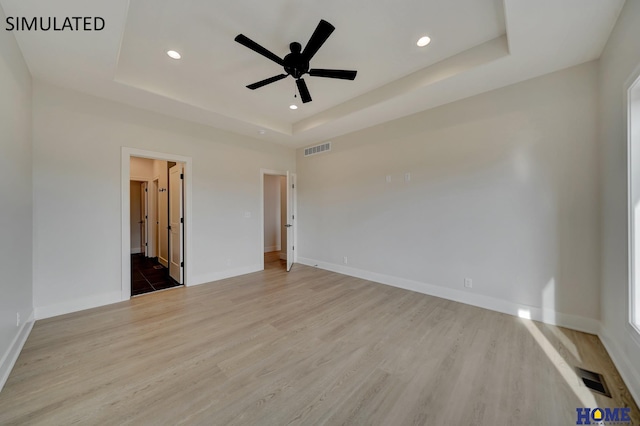 unfurnished bedroom with visible vents, a raised ceiling, and wood finished floors